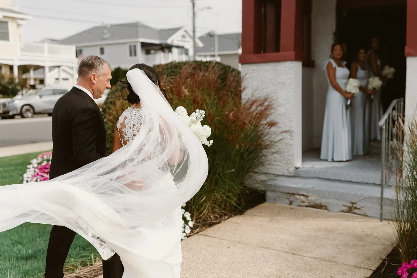 Morgan's veil catching the wind as her dad walks her to the door of Sacred Heart Church while her bridesmaids wait