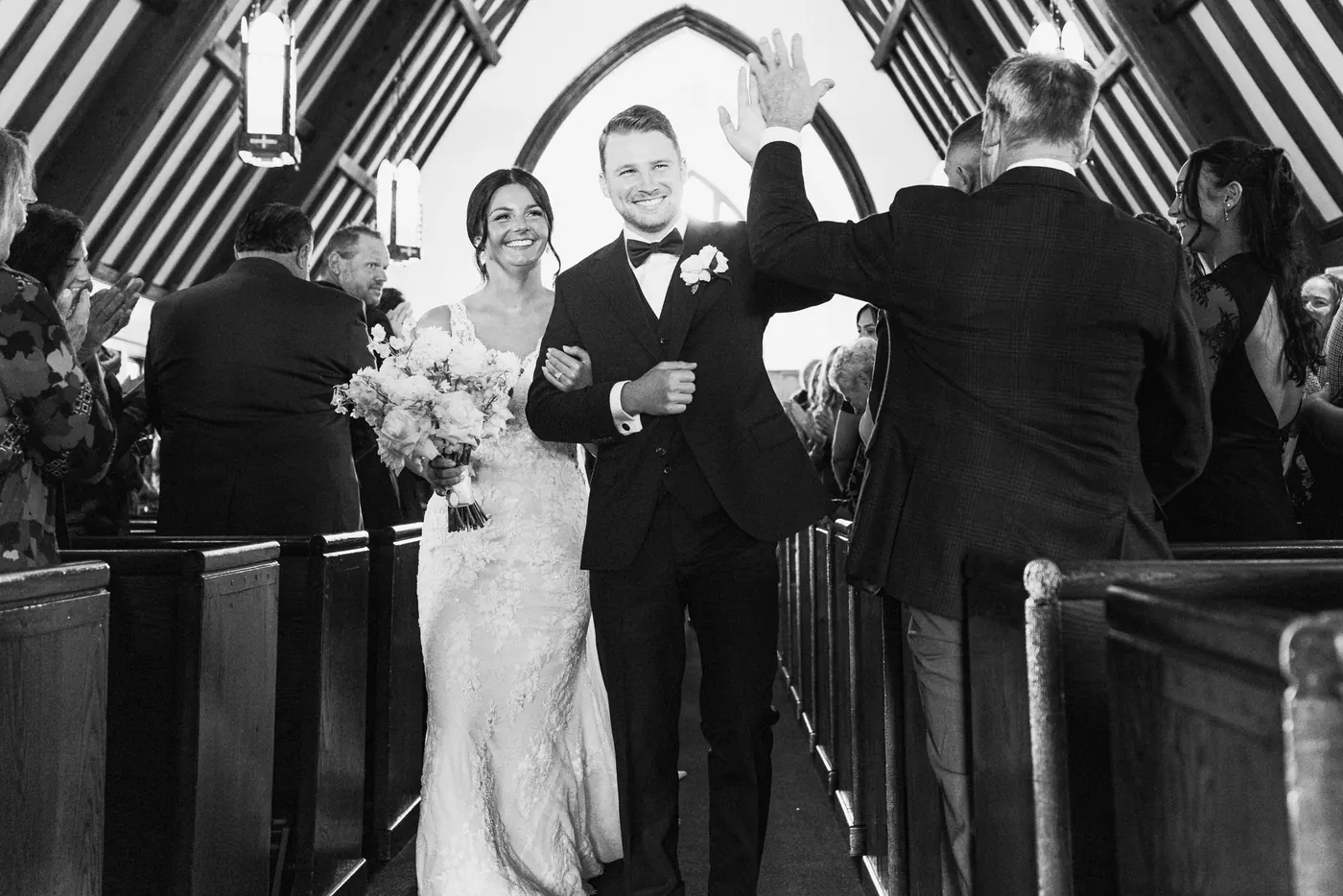 Black and white photo of Mason high-fiving a guest as he and Morgan walk back up the aisle