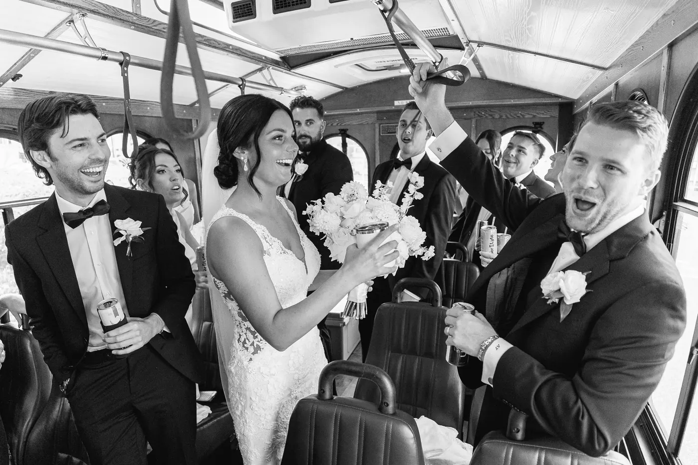 Black and white photo of Mason, Morgan and their wedding party cheering on the trolley ride