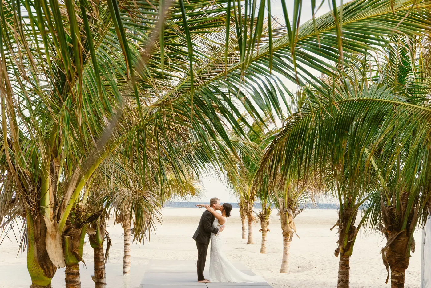 Mason and Morgan kissing among the palm trees on the beach at ICONA Diamond Beach