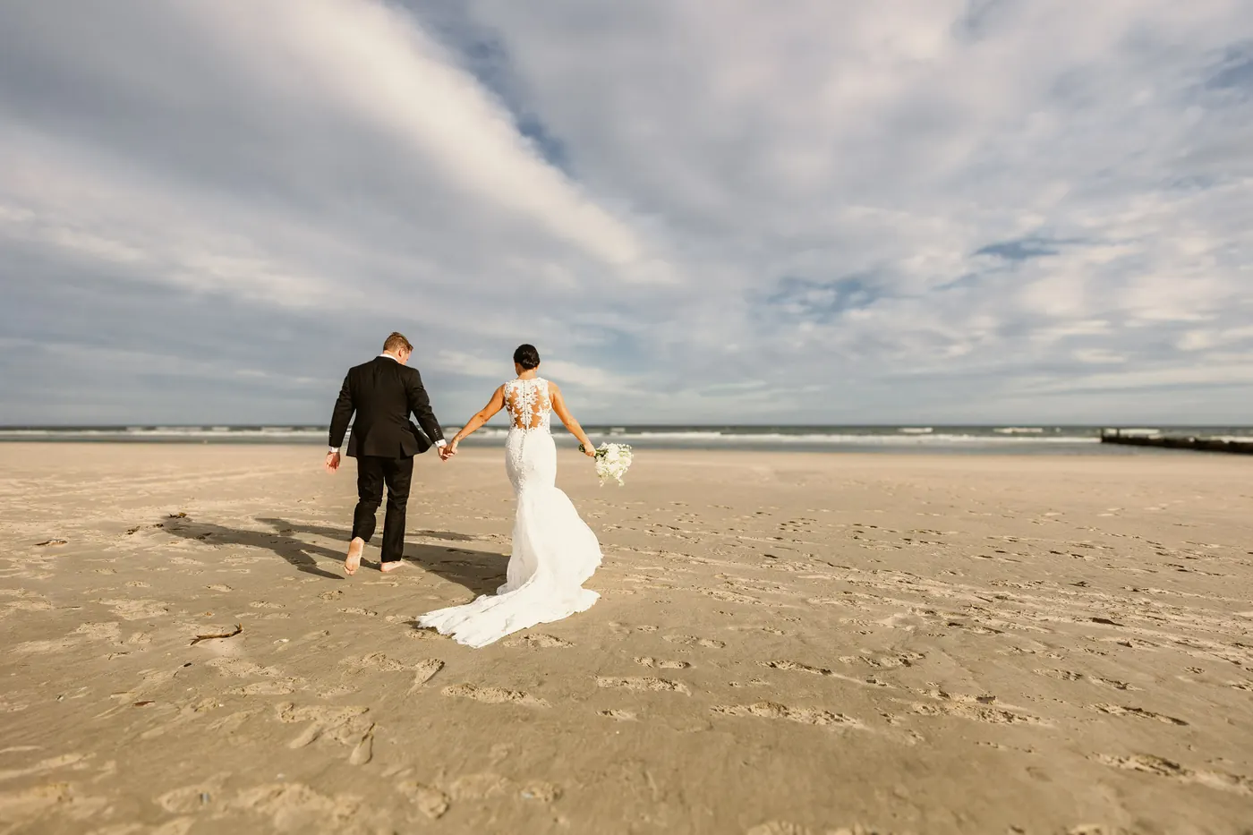 Mason and Morgan walking hand in hand across the wide beach toward the ocean