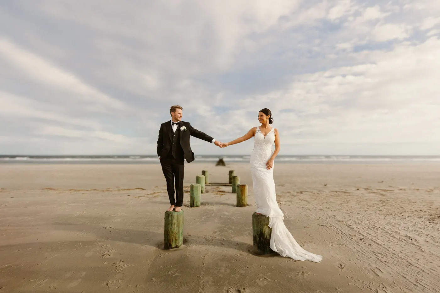 Mason and Morgan holding hands while standing on the posts of an old jetty on the beach