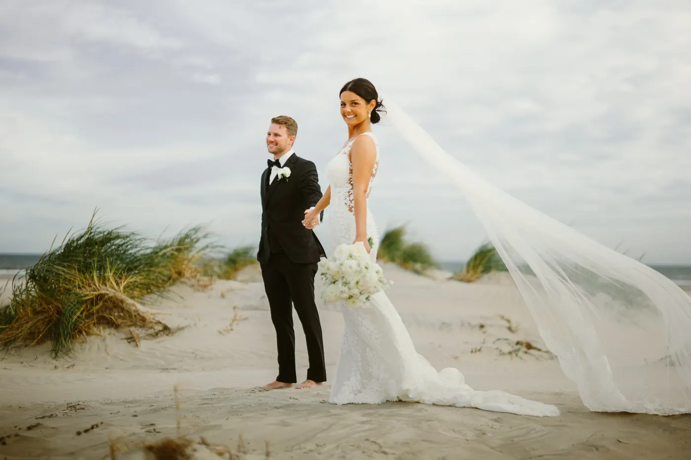 Mason and Morgan standing in the dunes with her veil streaming in the wind