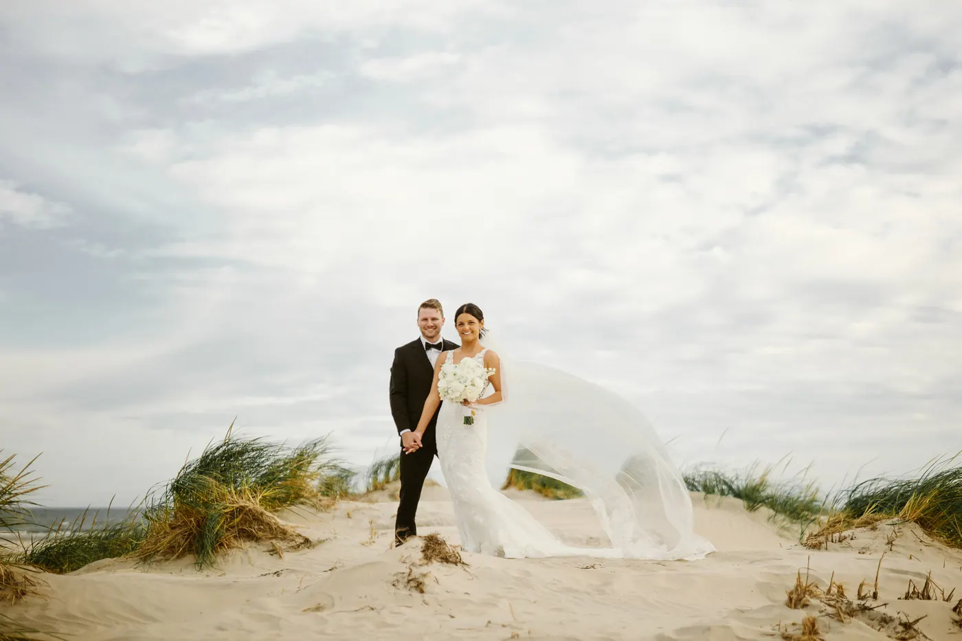 Mason and Morgan standing among the dune grass under a wide cloudy sky