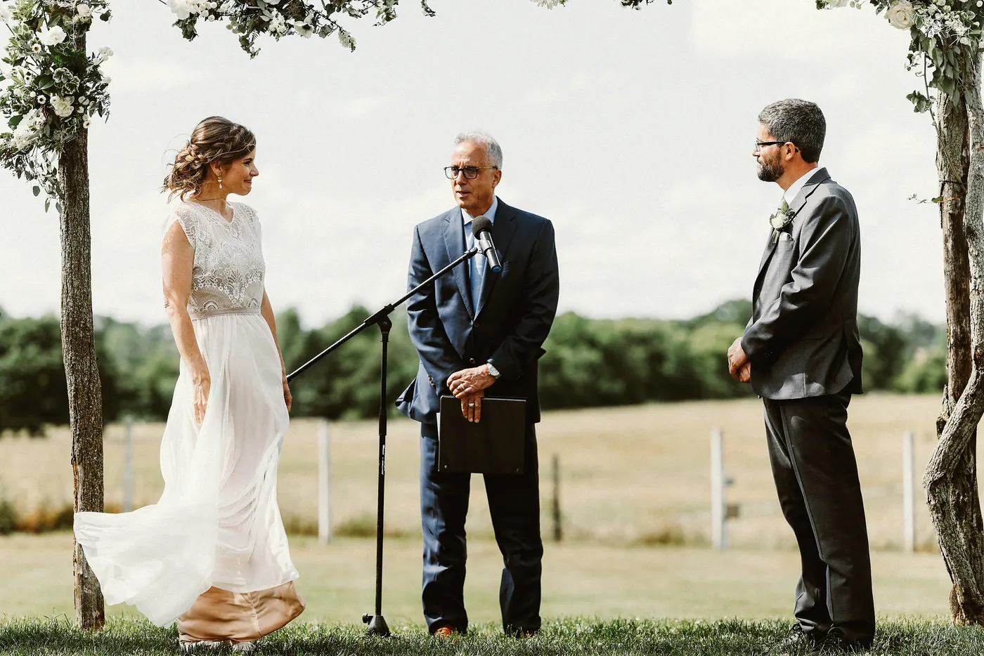 Matt and Erica facing each other under the wooden arbor during their ceremony at Johnson's Locust Hall Farm in Jobstown, NJ