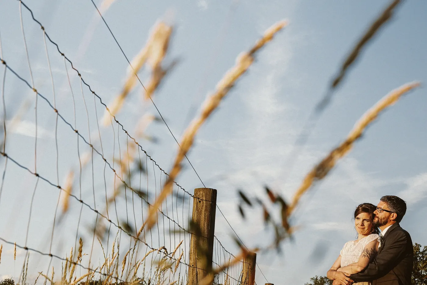 Matt and Erica by the wire fence with tall grass in the foreground at Johnson's Locust Hall Farm in Jobstown, NJ