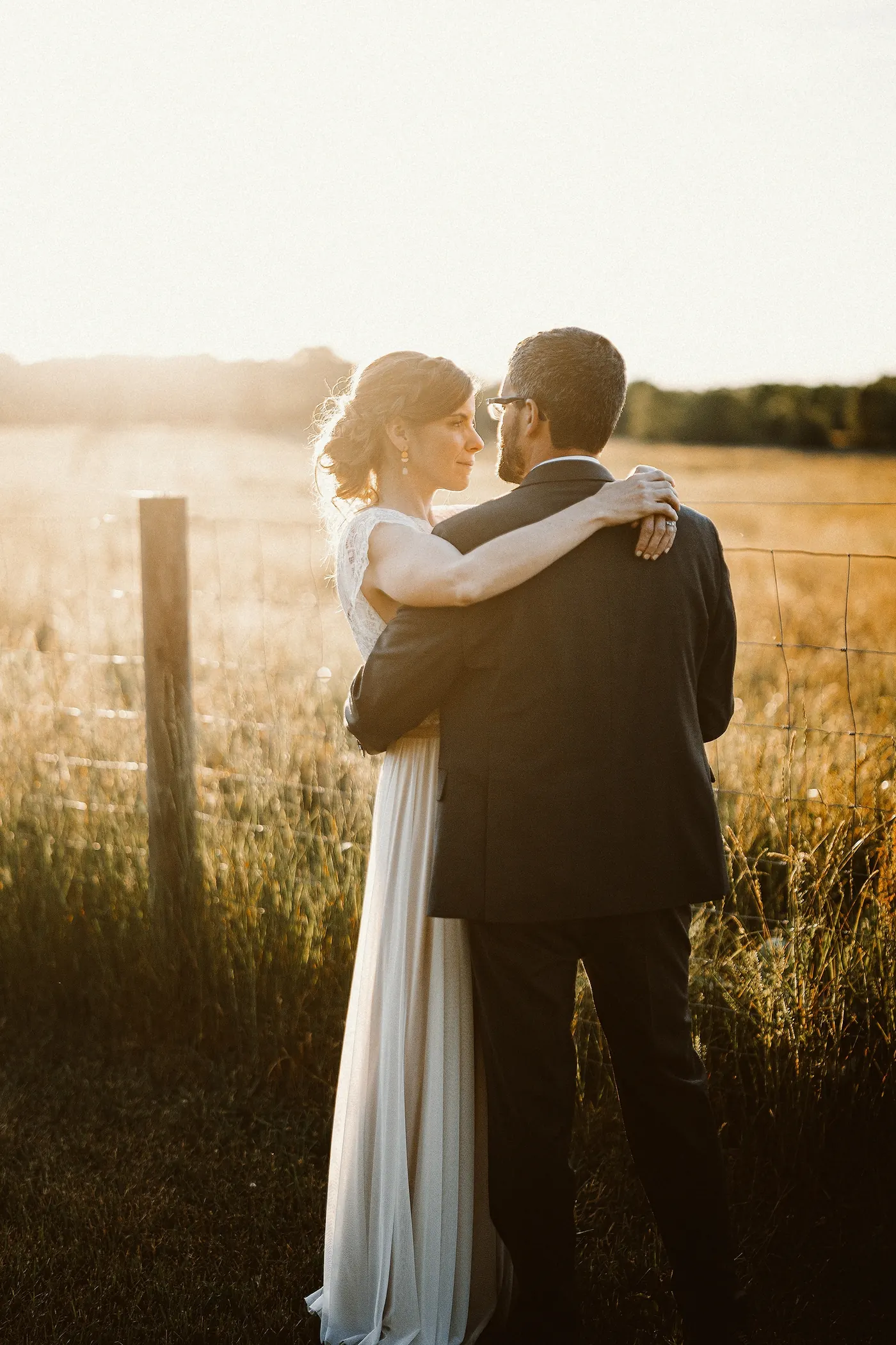 Matt and Erica embracing by the fence in golden hour light at Johnson's Locust Hall Farm in Jobstown, NJ