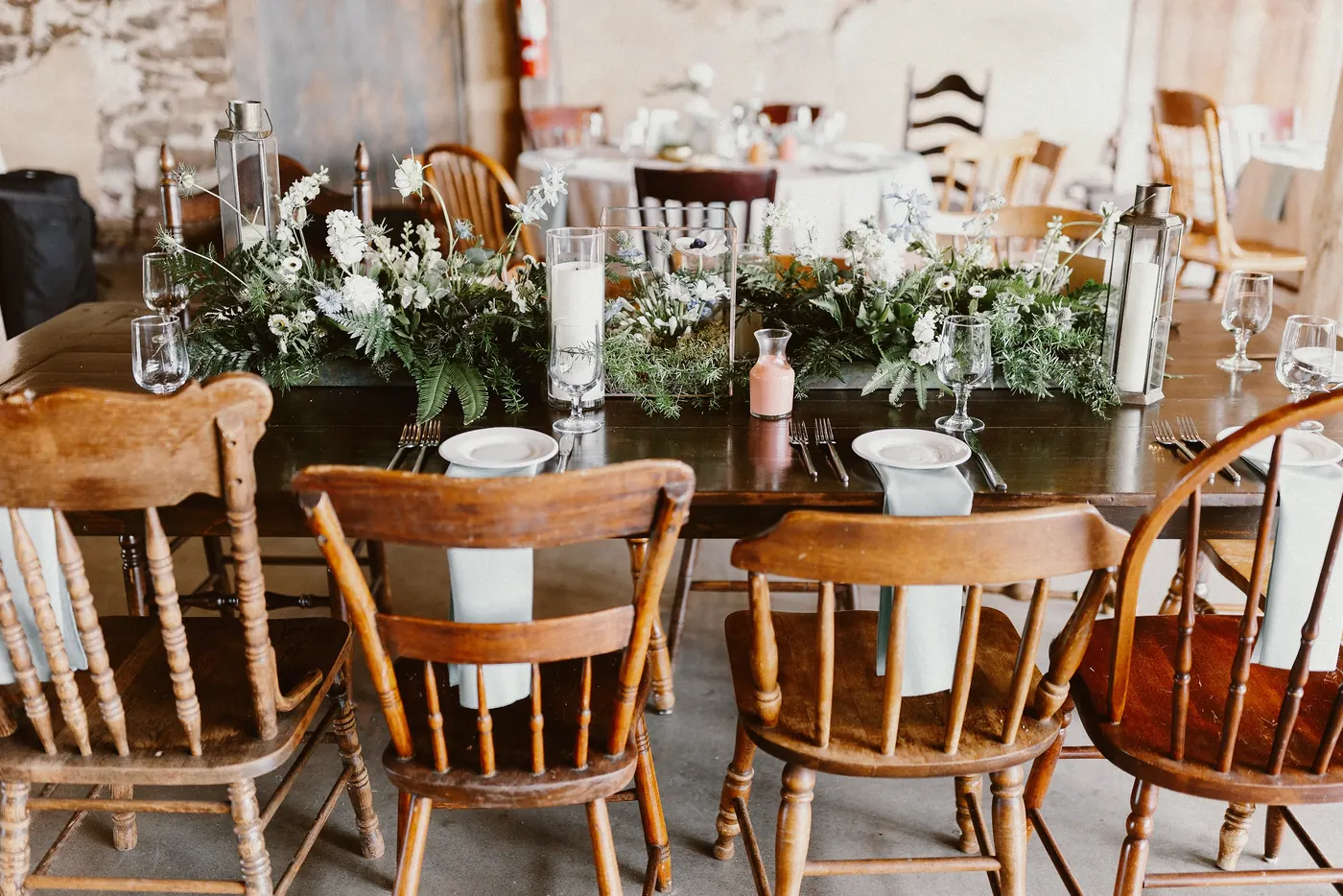 Long reception tables with mismatched wooden chairs and greenery in the barn at Johnson's Locust Hall Farm in Jobstown, NJ