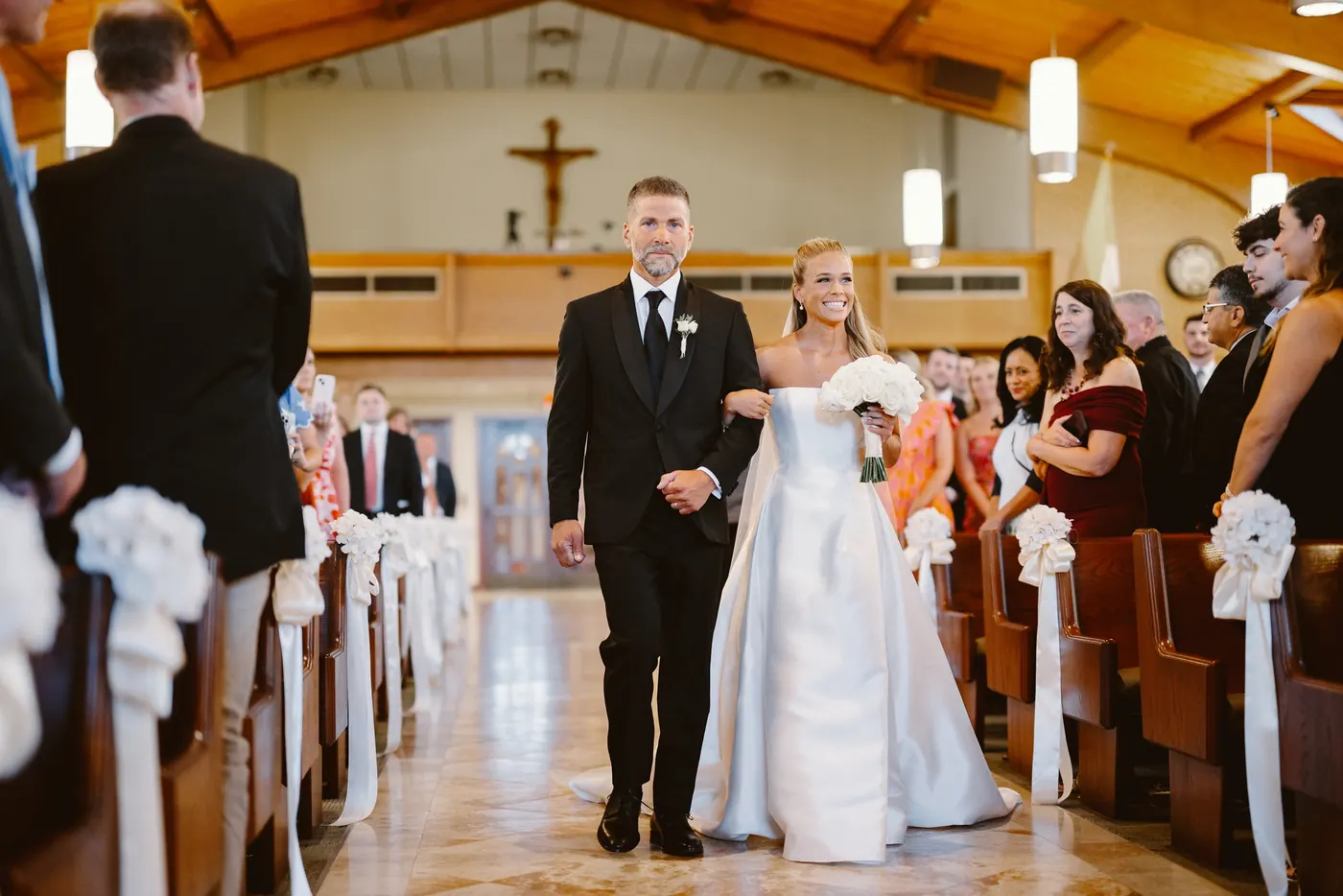 Madison smiling as she is walked down the aisle at Saint Charles Borromeo Church in Cinnaminson, NJ