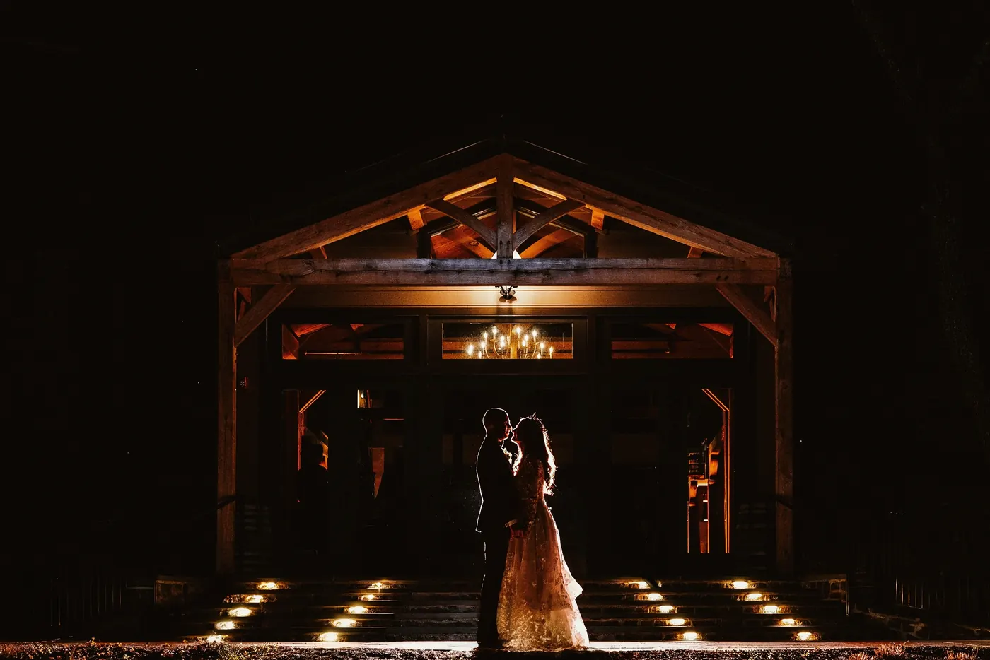 Steve and Maria embracing at night in the glowing entrance of the reception hall