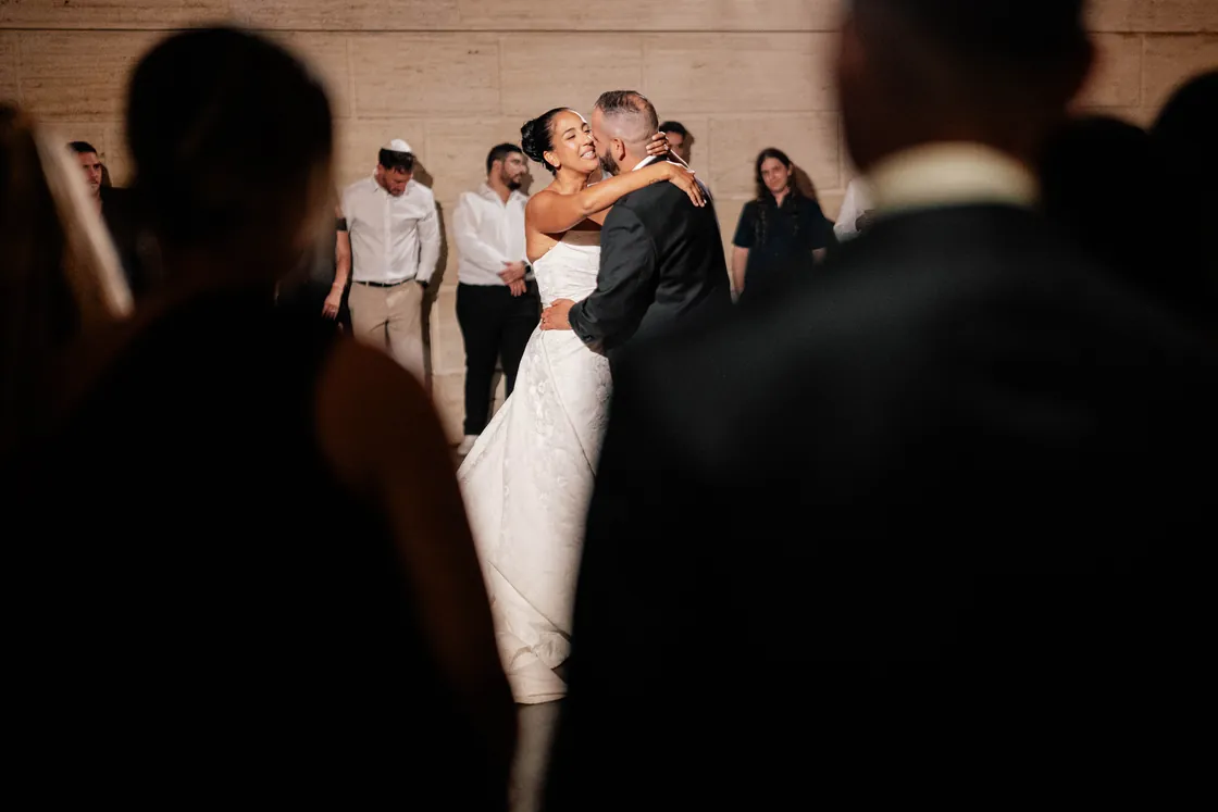 Gianna and Simon embracing during their first dance at the Union Trust in Philadelphia, framed by the silhouettes of their guests